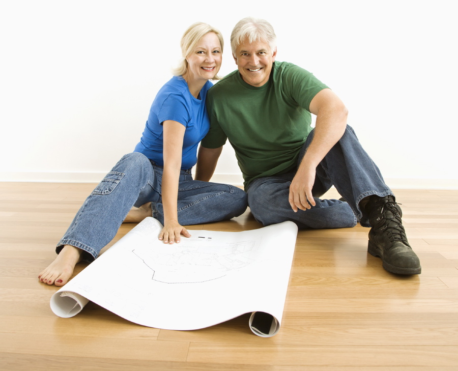 Photo of middle-aged couple sitting on floor with architectural blueprints